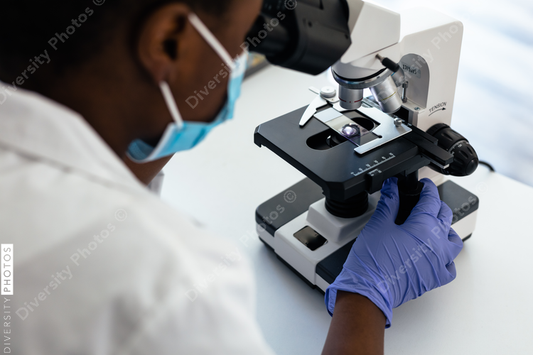 Black scientist and technician in mask in laboratory looking through microscope