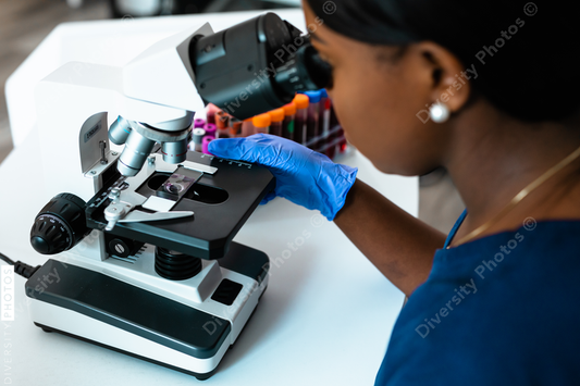 Black female medical professional in laboratory looking through microscope at blood samples