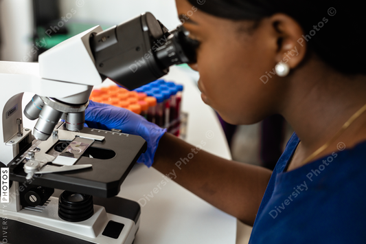 Black female medical professional in laboratory looking through microscope at blood samples