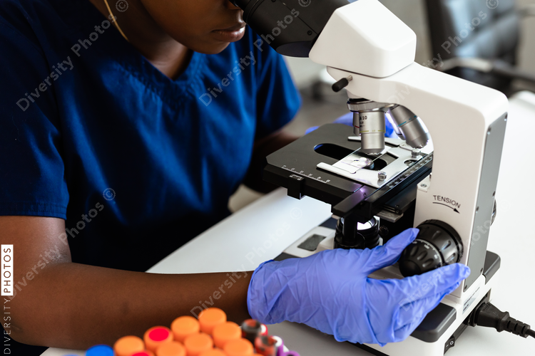 Black female medical professional in laboratory looking through microscope at blood samples