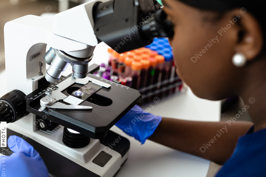 Black female medical professional in laboratory looking through microscope at blood samples