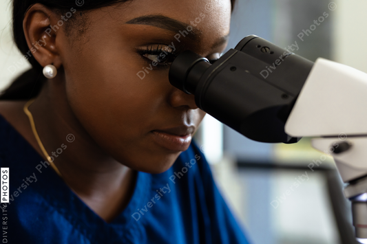 Black female medical professional in laboratory looking through microscope