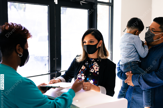 Black healthcare worker reviewing medical forms with Hispanic family at reception desk in doctor office