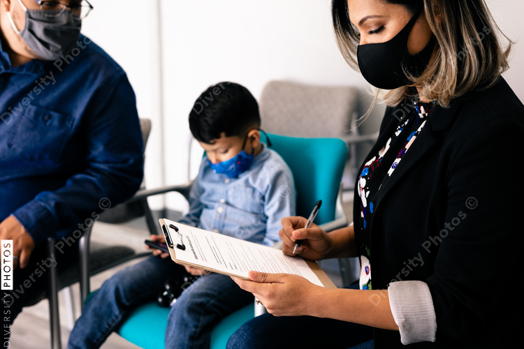 Latino family wearing masks completing medical forms in doctor office