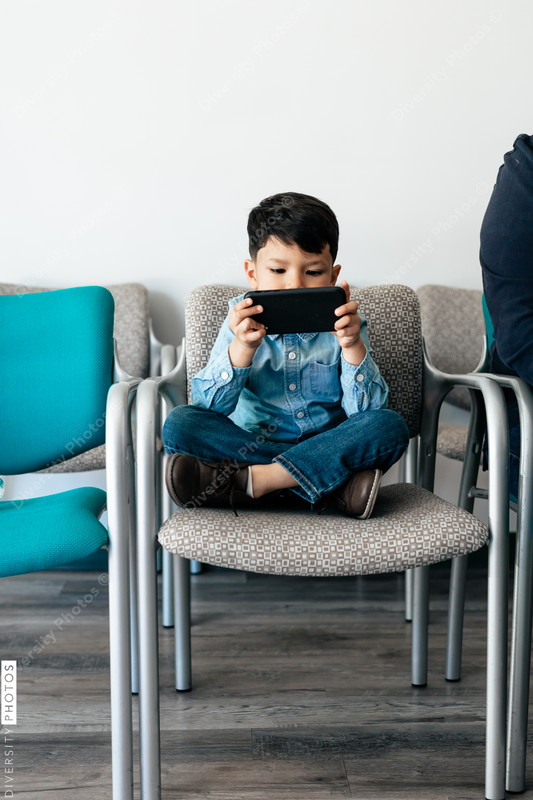 Young Hispanic toddler playing with phone in doctor office waiting room