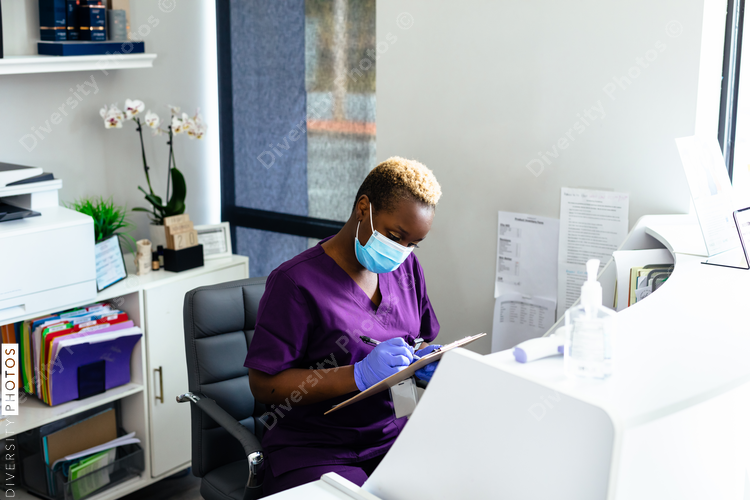 Black medical professional in mask at front desk in doctor office completing paperwork