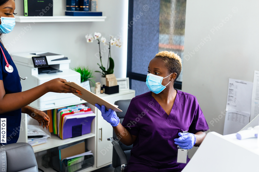 Black medical professional in mask at front desk in doctor office reviewing paperwork