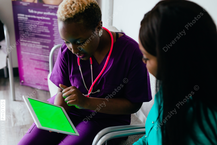 Black nurse reviewing information digitally on tablet with patient at medical facility