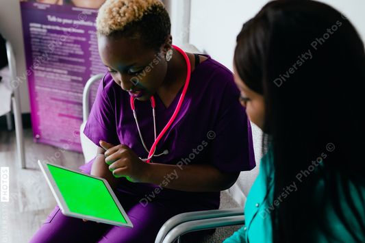 Black nurse reviewing information digitally on tablet with patient at medical facility