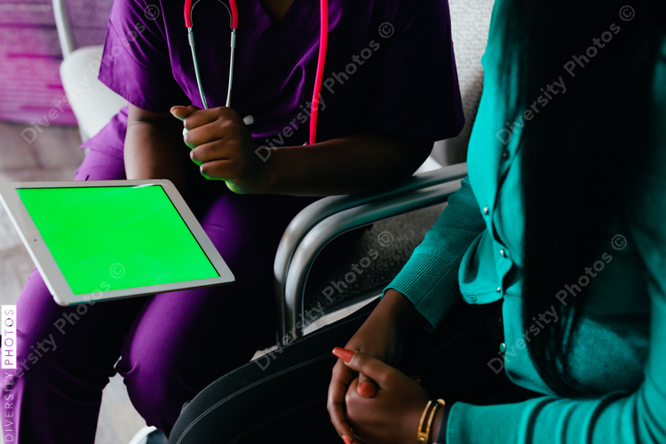 Black nurse reviewing information digitally on tablet with patient at medical facility