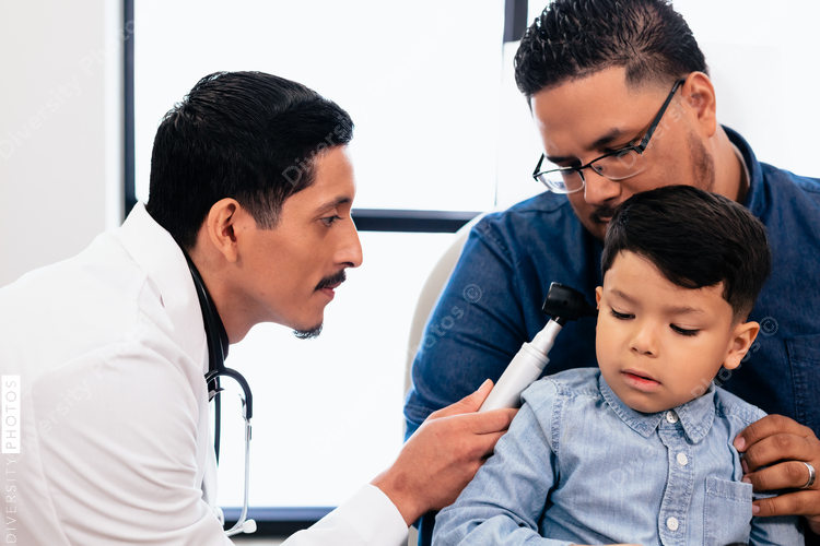 Doctor exams ears of young hispanic toddler with otoscope in medical exam room during wellness visit