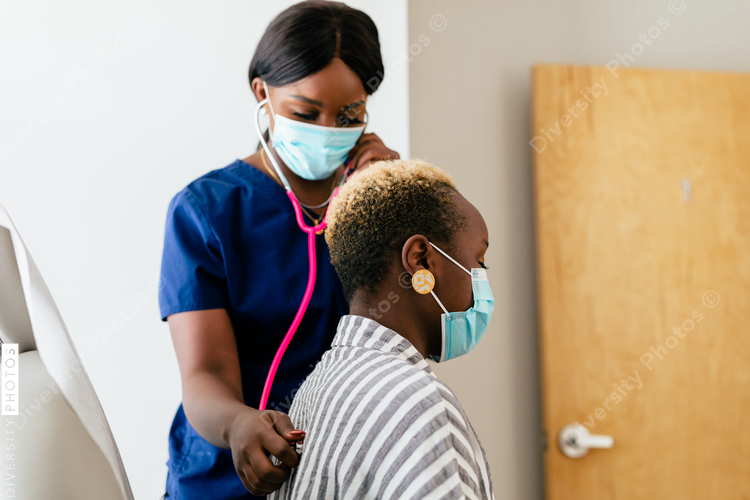 Black nurse takes vitals of black female patient in exam room at medical facility