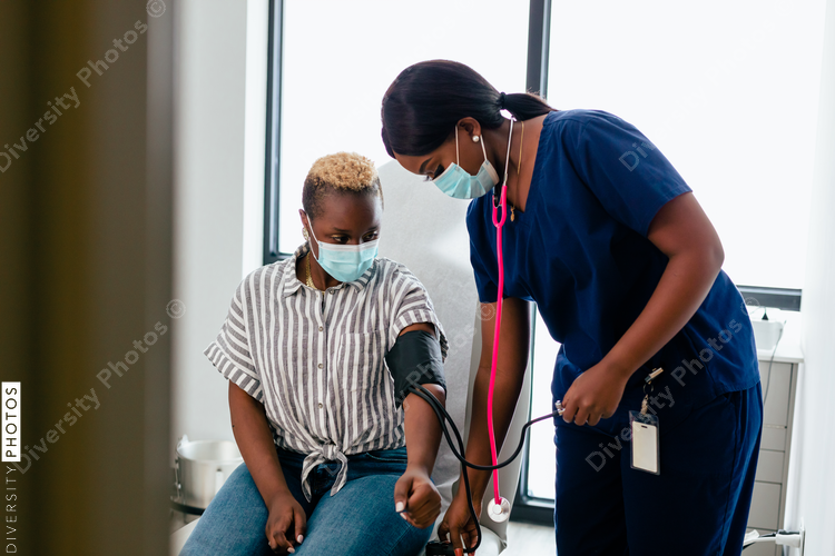 Black nurse takes blood pressure of black female patient in exam room at medical facility
