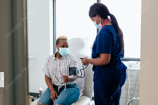 Black nurse takes blood pressure of black female patient in exam room at medical facility