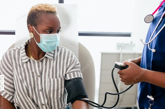 Black nurse takes blood pressure of black female patient in exam room at medical facility