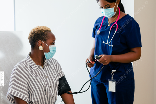Black nurse takes blood pressure of black female patient in exam room at medical facility