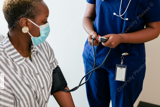 Black nurse takes blood pressure of black female patient in exam room at medical facility