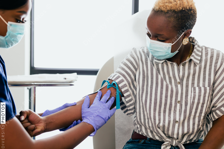 Black nurse collects blood sample from black female patient in exam room at medical facility