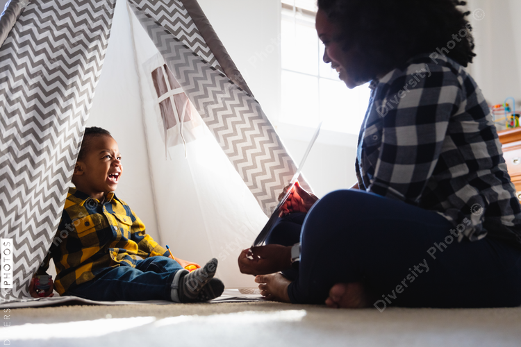 Mother teaching toddler at home sitting in tent in play room