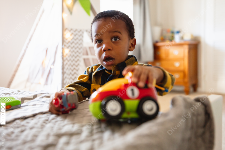 African American boy playing with new car toy at home in nursery