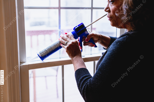 Black Senior woman weather sealing, caulking windows for winter