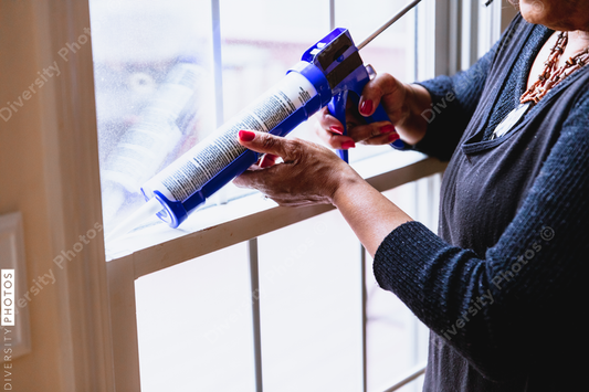 Black Senior woman weather sealing, caulking windows for winter