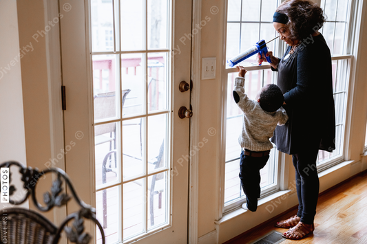 Black grandmother woman weather sealing, caulking windows for winter with toddler grandson