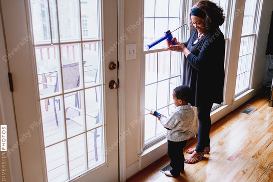 Black grandmother woman weather sealing, caulking windows for winter with toddler grandson