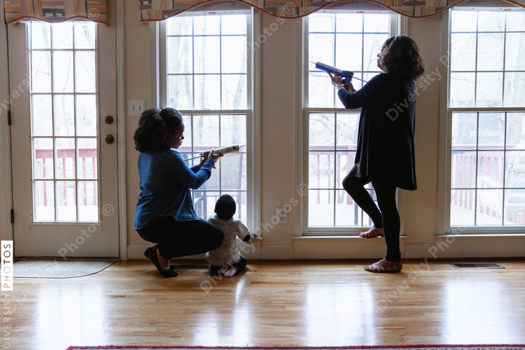 Multigenerational Black family caulking windows for home winter energy efficiency