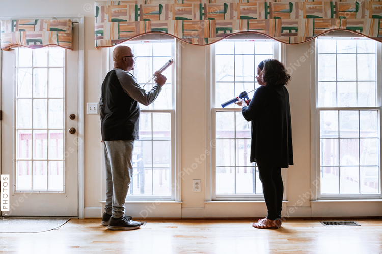 Senior retired husband and wife caulking windows for winter home energy efficiency