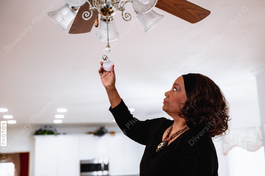 Black senior woman installing energy efficient LED light bults, DIY