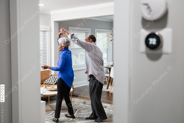 Black senior couple enjoys retirement at home dancing to music, smart thermostat