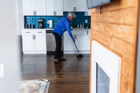 Black senior woman sweeping kitchen and cleaning up home