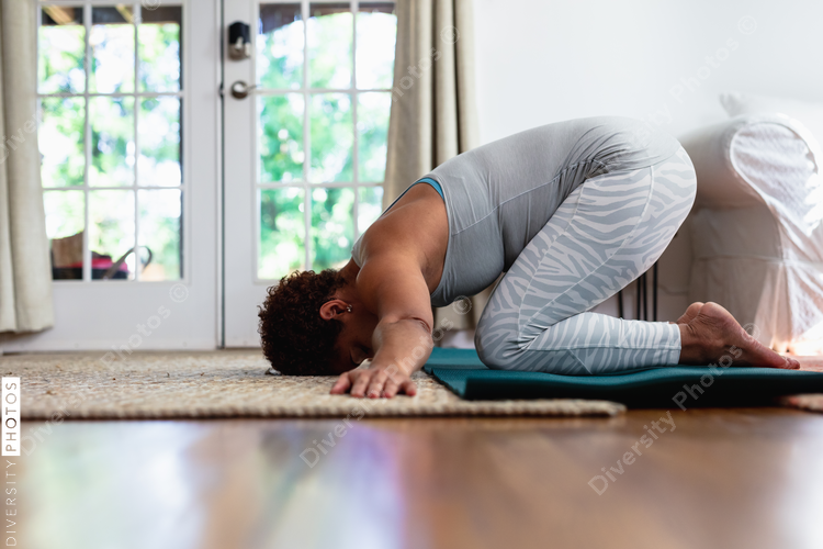 Mature Black woman does downward dog pose in yoga mat, humble