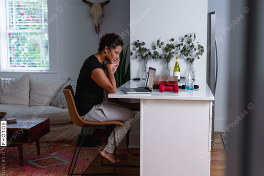 African-American woman works on laptop in home kitchen