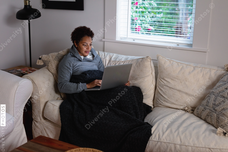 Black woman checking messages on laptop at home on couch