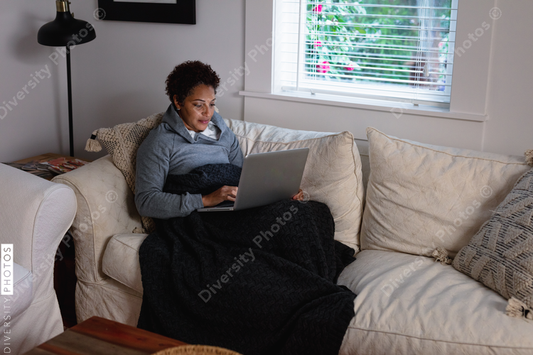Black woman checking messages on laptop at home on couch
