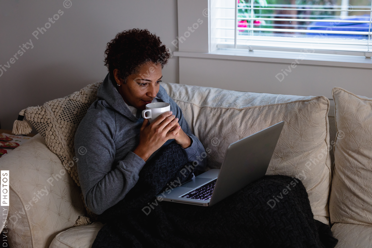 Black woman drinking tea on couch snuggled and warm