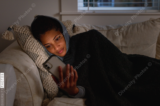 Black woman cozy on sofa checking cellphone