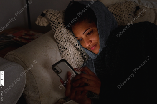 Black woman cozy on sofa checking cellphone