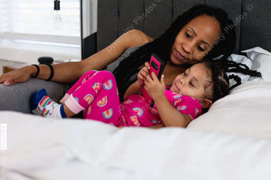Black mom and daughter in bed watching show on phone