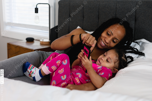 Black mom and daughter in bed watching show on phone