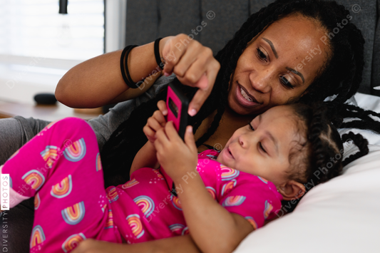 Black mom and daughter in bed watching show on phone