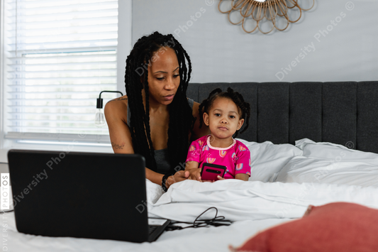 Black Mom working remotely in bed with child