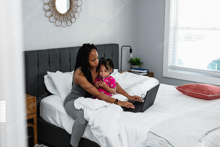 Mom working in bed on laptop with toddler