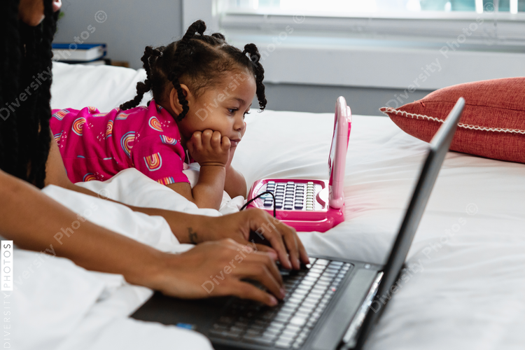 Toddler on toy laptop next to mother who is working from home