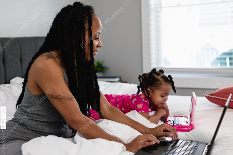Toddler on toy laptop next to mother who is working from home