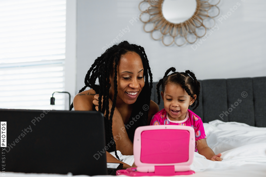 Black mother and daughter plays on toy laptop while working from home remotely