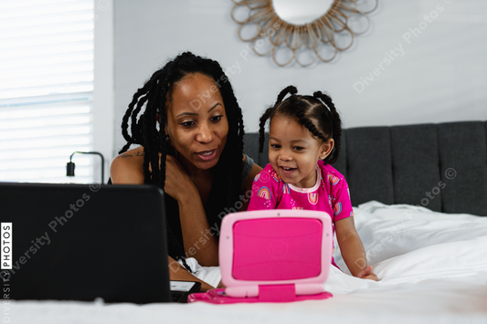 Black mother and daughter plays on toy laptop while working from home remotely