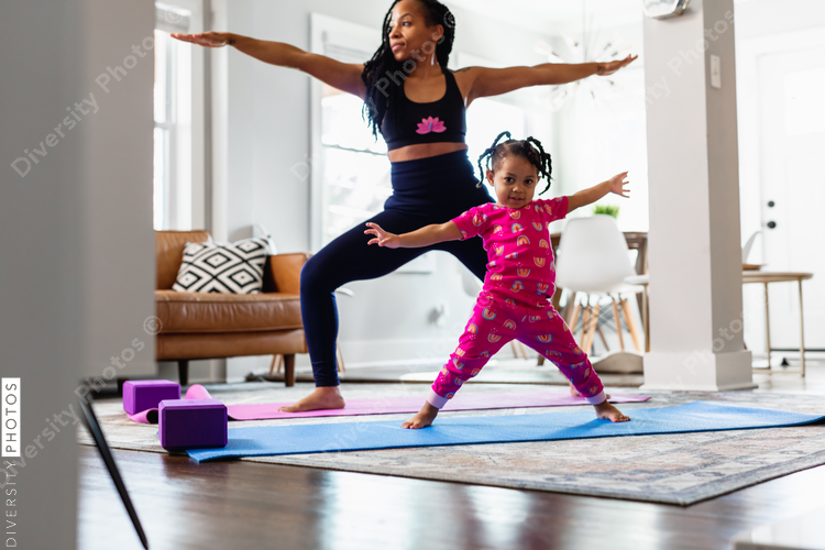 Black Mother and daughter doing yoga in family room, warrior pose